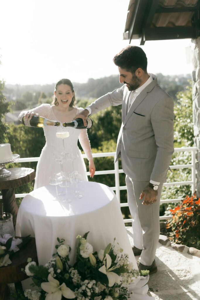 Champagner Tower Hochzeit: Brautpaar gießt prickelnden Schaumwein in den kaskadierenden Turm.